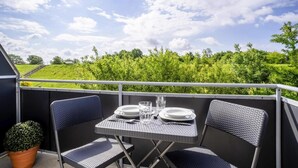 A balcony with a table set for two, two chairs, and a potted plant.