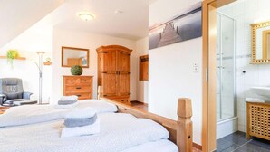 A hotel room with two beds, a wooden wardrobe, a mirror, and a shower area.