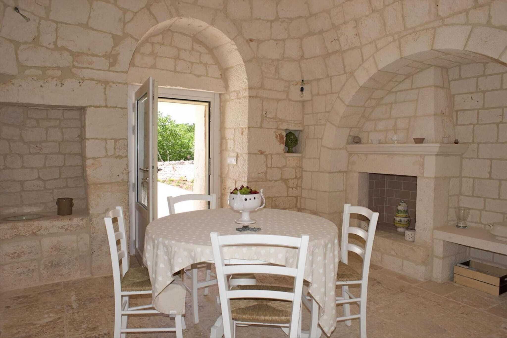 Una habitación de paredes de piedra con una mesa redonda y sillas blancas, una chimenea y una puerta que da al exterior.