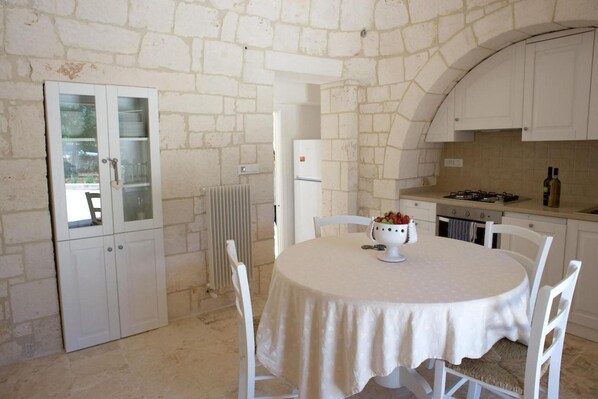 A kitchen with white cabinets, a round table with a white tablecloth, and a bowl of fruit.