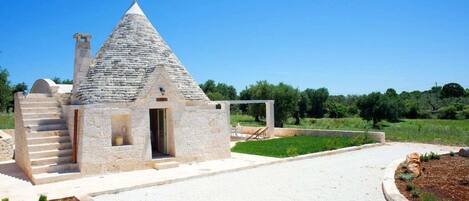 A stone building with a conical roof, a staircase, and a garden area.