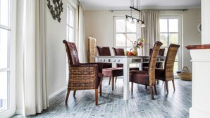 Un coin repas avec une table blanche, des chaises marron et un vase rempli de fleurs.