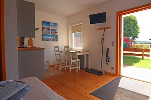 A room with a bed, a desk with chairs, a window, and a door leading to an outdoor area.