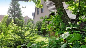 A house with a sloped roof, surrounded by lush greenery and trees. - Ferienhaus mit Garten in Nessmersiel (Neßmersiel)