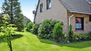 A two-story house with a sloped roof, a satellite dish, and a well-maintained garden with various shrubs and a lawn. - Ferienhaus mit Garten in Nessmersiel (Neßmersiel)