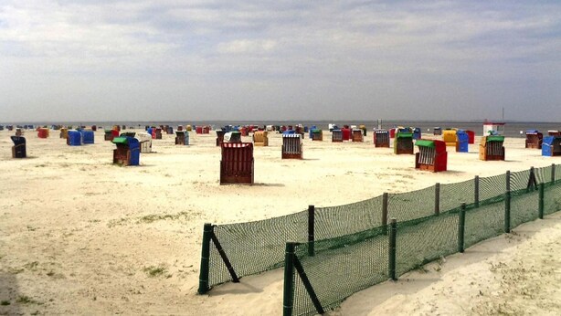 A sandy beach with a green fence and colorful containers lined up. - Ferienhaus mit Garten in Nessmersiel (Neßmersiel)