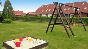 A playground with a wooden swing set and a sandbox with sand and toys. - Ferienhaus mit Garten in Nessmersiel (Neßmersiel)