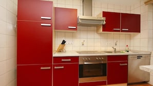 Una cocina con armarios rojos, horno de acero inoxidable y lavavajillas.