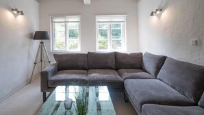 A modern living room with a sectional sofa, a glass coffee table, and two windows with white frames. - Stylische Ferienwohnung in ländlicher Idylle (Wobbenbüll)