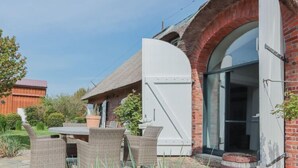A brick house with a large white door, outdoor wicker furniture, and a garden area. - Stylische Ferienwohnung in ländlicher Idylle (Wobbenbüll)