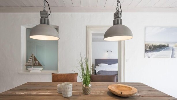A wooden dining table with two pendant lights, a potted plant, and a decorative bowl. - Stylische Ferienwohnung in ländlicher Idylle (Wobbenbüll)