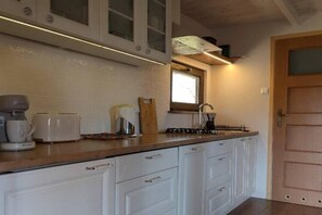 Una cocina con armarios blancos, encimera de madera, cafetera, tostadora y ventana sobre el fregadero.