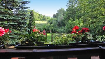 A garden with potted plants and flowers, a wooden bench, and a view of a green field and trees.