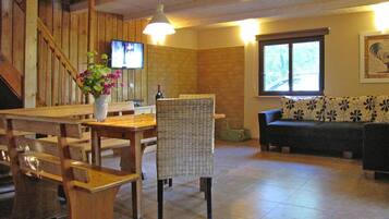 A dining area with a wooden table, chairs, a vase with flowers, a television, and a sofa with a floral pattern.