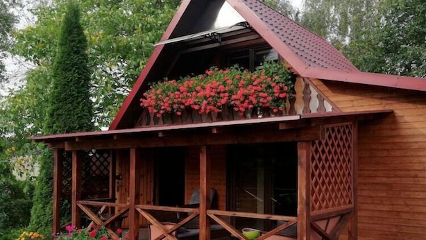 A wooden cabin with a porch, a covered area with red flowers, and a lattice fence. - Holiday home with jacuzzi and private garden (Gizycko)