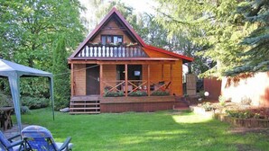 A wooden cabin with a porch, surrounded by a well-maintained lawn and trees. - Holiday home with jacuzzi and private garden (Gizycko)