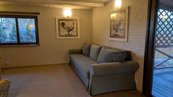 A room with a grey sofa, two framed pictures on the wall, a window, and a door leading outside.