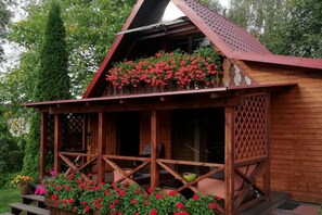 A wooden cabin with a porch, a covered outdoor seating area, and a flower box with red flowers. - Holiday home with jacuzzi and private garden (Gizycko)