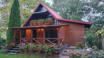 A wooden cabin with a porch, surrounded by a garden with various plants and flowers.