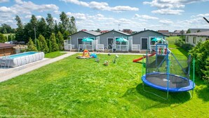 A residential backyard with a swimming pool, trampoline, and play area.