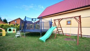 Un jardin avec un trampoline, un toboggan, une balançoire et une petite cabane de jeux.