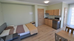 Une pièce de taille modeste comprenant un lit, une petite kitchenette, un coin repas et une porte donnant sur une autre pièce.
