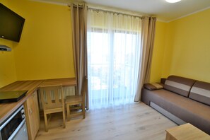 A living room with a sofa, a dining table with chairs, a television, and a window with curtains. - Holiday studio near the beach, playground (Sarbinowo)