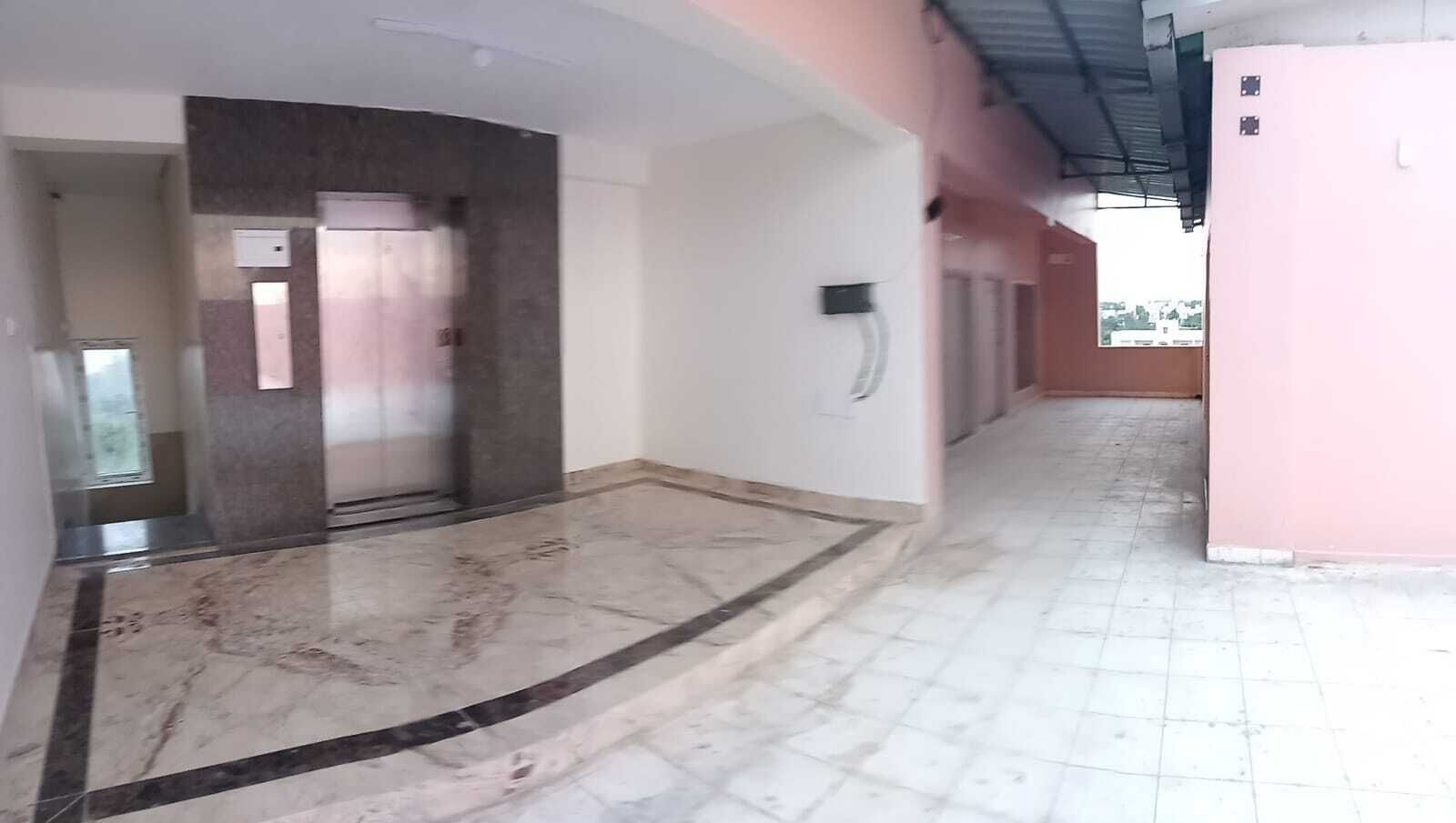 Um corredor com piso de mármore, uma porta e um interfone fixado na parede.