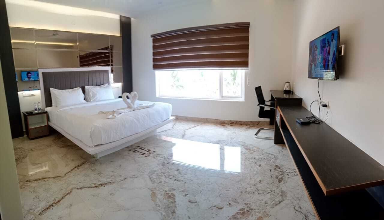 Une chambre d’hôtel moderne équipée d’un grand lit, d’un bureau, d’une télévision et d’une fenêtre avec des stores.