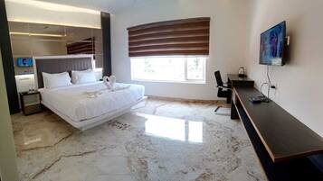 A modern hotel room with a large bed, a desk, a TV, and a window with blinds.