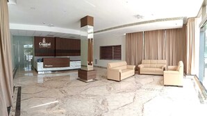 Un vestíbulo de hotel con un mostrador de recepción, una gran columna de madera vertical y tres sofás color beige.