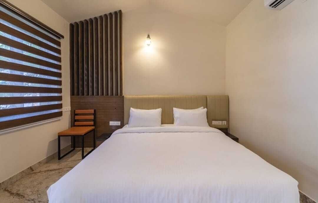 Una habitación de hotel con una cama grande, un cabecero de madera, una mesita de noche, una silla y una ventana con persianas.