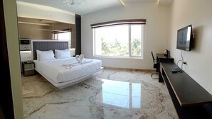Una habitación de hotel moderna con una cama grande, televisión, escritorio y ventana con vistas a zonas verdes.