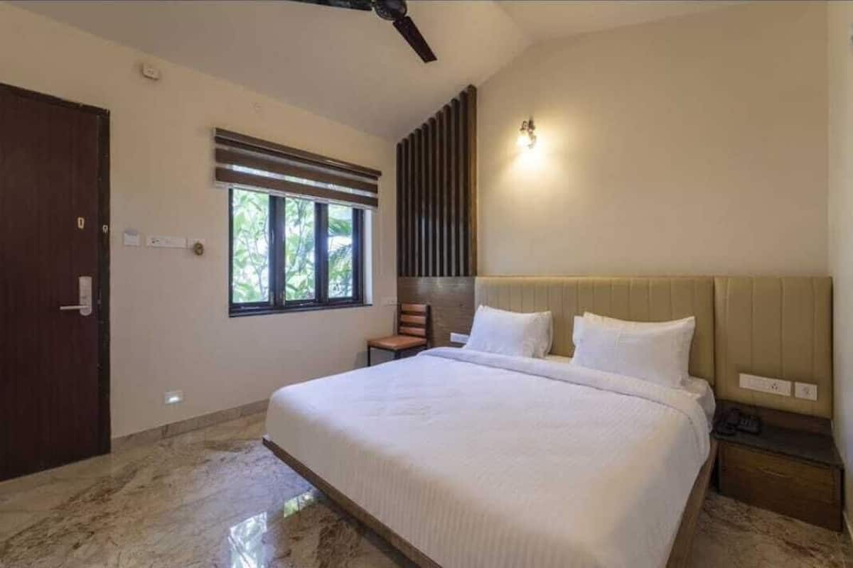 A bedroom with a large bed, a window with blinds, a ceiling fan, and a nightstand.