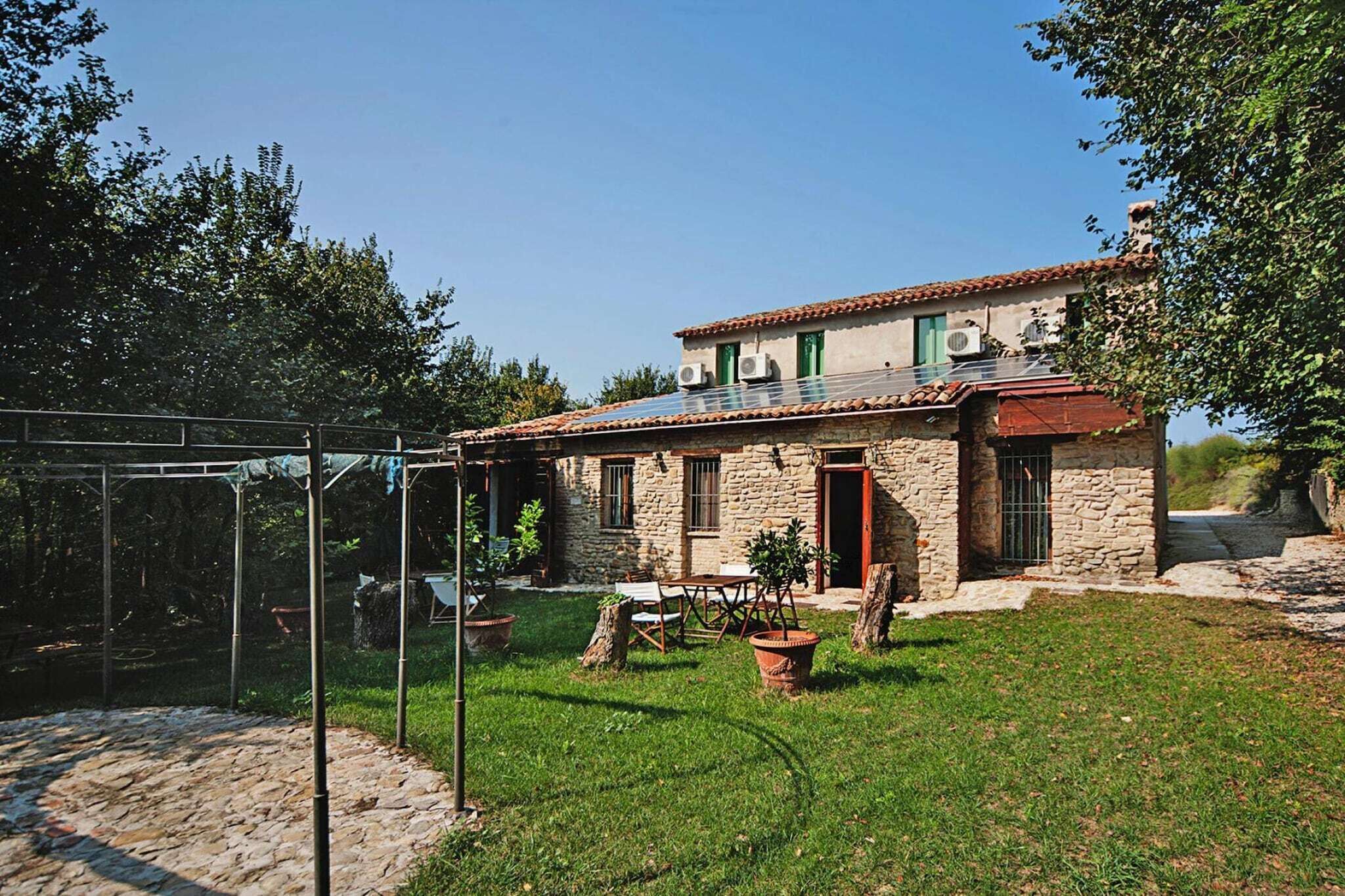 Ein Steinhaus mit Ziegeldach, ein Garten mit Tisch und Stühlen sowie eine Pergola.