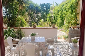 Une terrasse extérieure avec une table et des chaises, entourée de plantes en pot et d’une variété de verdure.