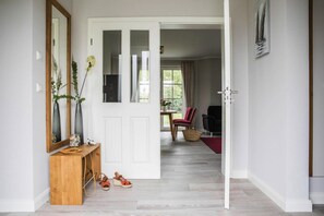 Ein Flur mit einem Holzkonsolentisch, einem Spiegel und einer Tür zu einem Raum mit einem roten Sessel und einem Korb.