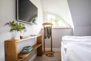 Ein Schlafzimmer mit einem Bett, einer Holzregal mit Büchern, einem Kleiderständer und einem Fenster mit Pflanzen.