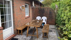 Een bakstenen huis met een terras, compleet met een houten tafel en twee witte plastic stoelen.