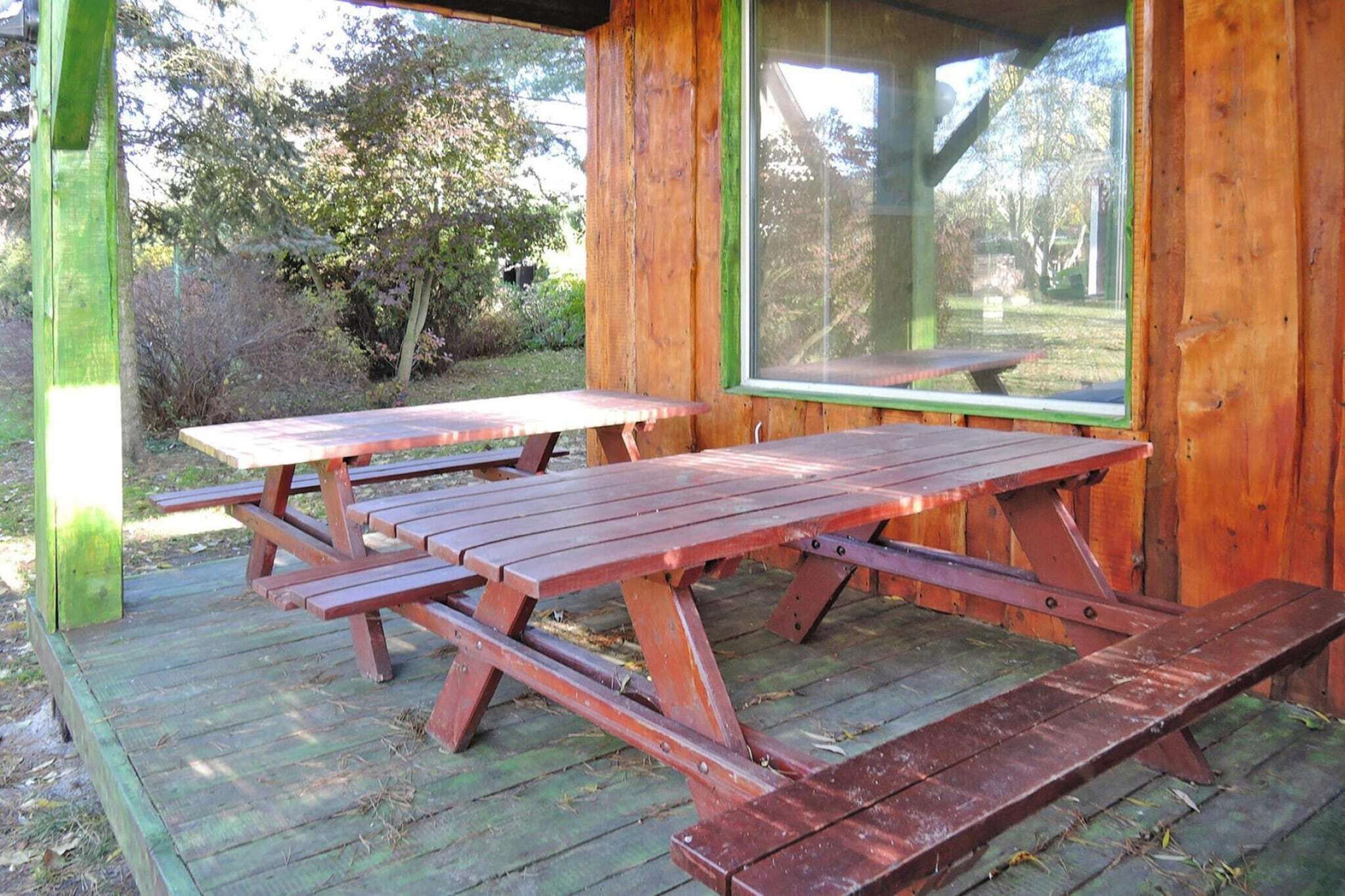 Una mesa de picnic de madera con bancos, ubicada en una terraza de madera con vistas a árboles y césped.
