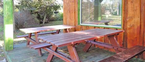 Una mesa de picnic de madera con bancos, ubicada en una terraza de madera con vistas a árboles y césped.