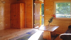 L’intérieur d’un chalet en bois, avec un plancher en bois, une table ornée d’un vase et une fenêtre donnant sur des arbres.
