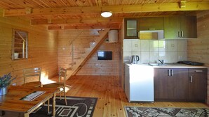 L’intérieur d’une cabane en bois comprend un coin cuisine, une table à manger avec des chaises et un escalier menant à un niveau supérieur.