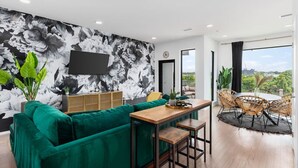 Ein modernes Wohnzimmer mit einem grünen Sofa, einem Holzespeisesaal mit Stühlen und einem großen floralen Wandbild.
