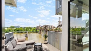 Ein Balkon mit einer Couch, einem runden Tisch und Blick auf eine Brücke und Grünflächen.