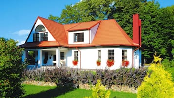 A two-story house with a red roof, white walls, and a garden with various plants and flowers.