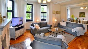 A living room with a television, sofas, a coffee table, and a dining area with chairs and a table.