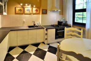 A kitchen with a black and white checkered floor, a sink, a stove, and a dining table with a chair.