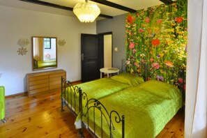 A bedroom with two beds, a dresser, a mirror, a small table, and a floral wall tapestry.
