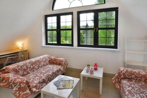 Une pièce comprenant un canapé, une petite table, une lampe et une fenêtre donnant sur un paysage verdoyant.